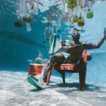 man sitting on chair underwater with floating bottles